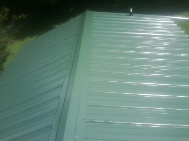 New green metal panels meeting at the ridge of a roof — Flat Roof Repair work by our crew in Newfoundland