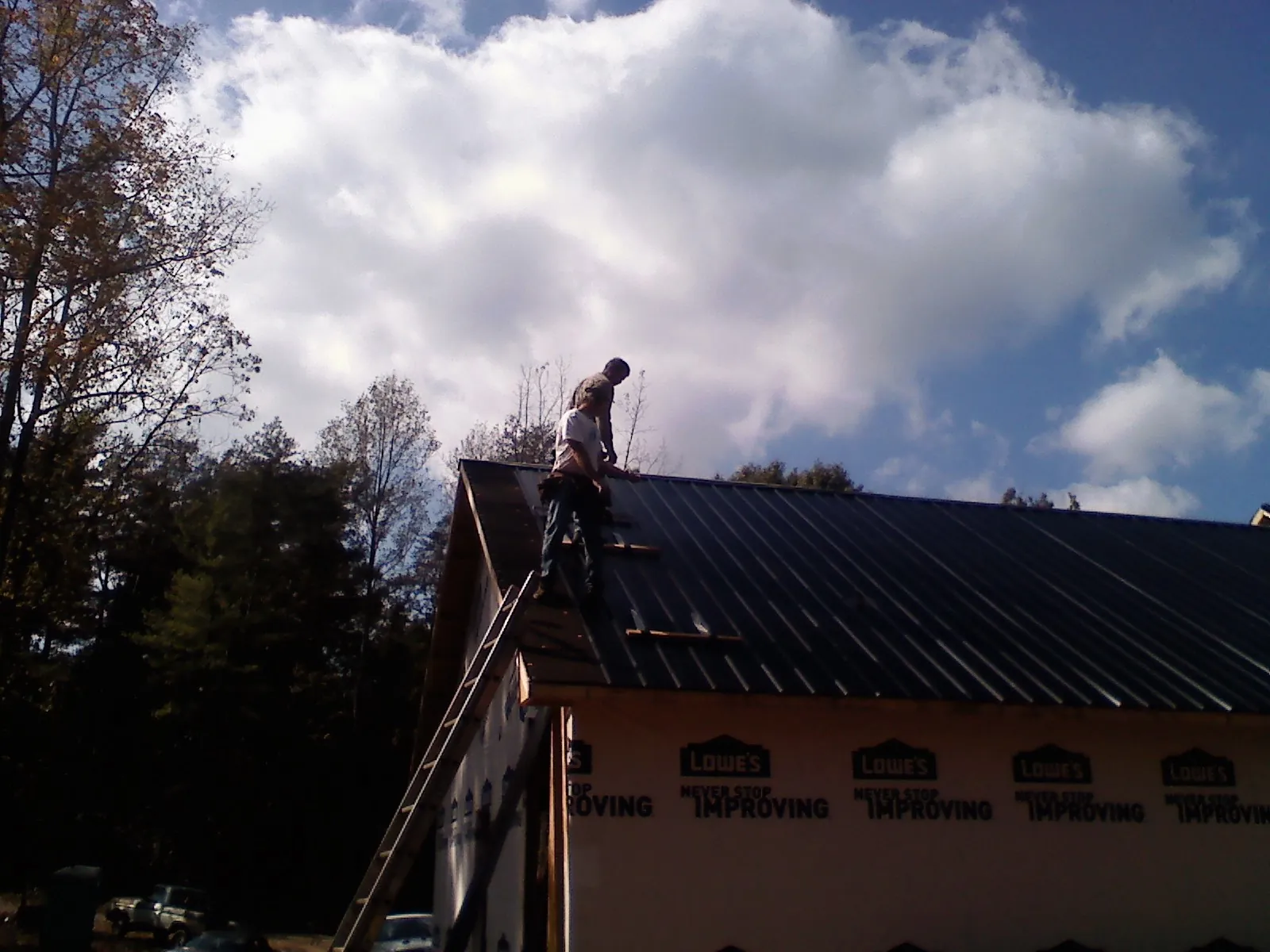 Roofer fastening dark metal panels high against a cloudy sky, from a Roof Inspection job in Newfoundland