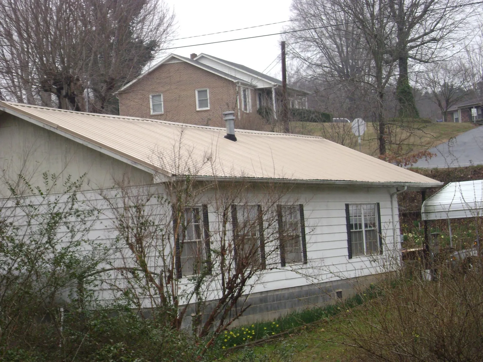 Tan metal roof on a white sided house set into a hillside — Commercial Roofing by Roofing Brothers in Newfoundland