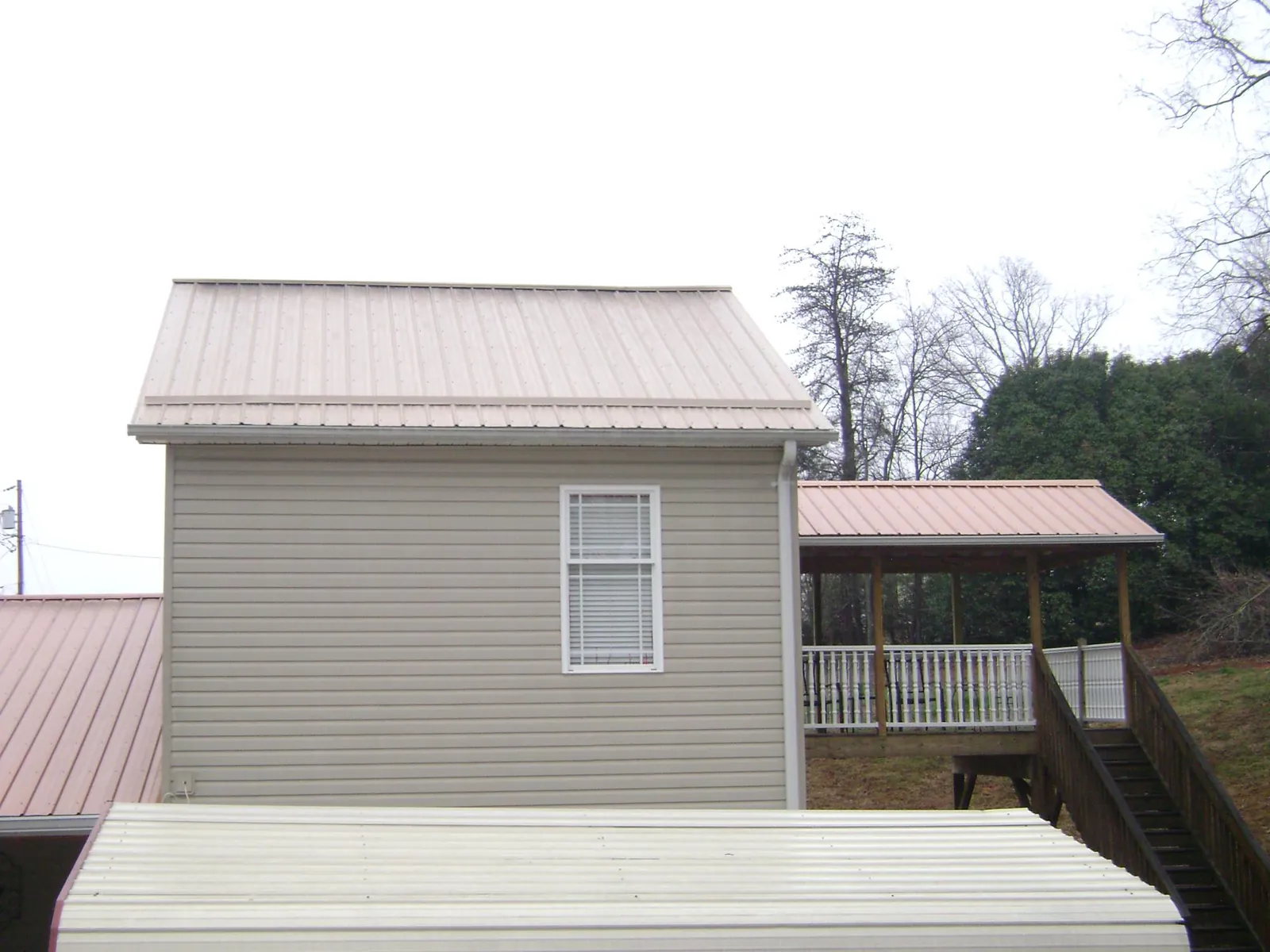 Tan metal roofs on a two story addition and attached porch, from a Roof Replacement job in Newfoundland